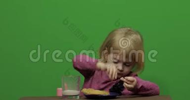 女孩坐在桌子旁<strong>吃</strong>巧克力、<strong>饼干</strong>和饮料可可。 快乐的三岁女孩。 可爱的女孩<strong>微笑</strong>